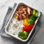 Three chicken and rice gluten-free meal prep bowls with vegetables and sauce, clean kitchen background