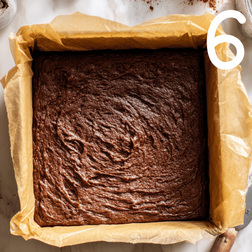 Top down view of thick pumpkin brownie batter spread evenly in an 8x8 inch parchment-lined pan on a marble countertop