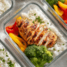 Chicken and rice gluten-free meal prep containers with fresh vegetables on a bright kitchen counter