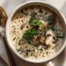 Top-down view of a steaming bowl of gluten-free creamy mushroom soup garnished with parsley and black pepper on a wooden table