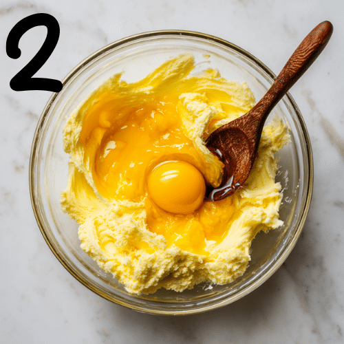 Overhead shot of creamed butter and sugar in a glass bowl with egg yolk, pumpkin puree, and vanilla extract being added, autumn baking scene
