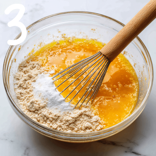 Mixing wet and dry ingredients for pumpkin brownies in a glass bowl on a marble counter