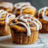 Pumpkin Cinnamon Roll Muffins on a marble table with cream cheese drizzle, bright morning light, high detail food photography