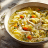 Cozy bowl of chicken noodle soup with egg noodles on a rustic wooden table, garnished with parsley