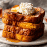 Golden Pumpkin French Toast on a marble plate topped with whipped cream, maple syrup, and autumn leaves