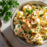 Top-down view of a creamy potato salad in a rustic bowl, garnished with parsley and paprika, surrounded by boiled eggs and celery
