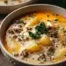 Bowl of Cheesy Hamburger Potato Soup topped with cheese and herbs