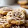 Freshly baked cinnamon roll cookies drizzled with icing on a cooling rack.