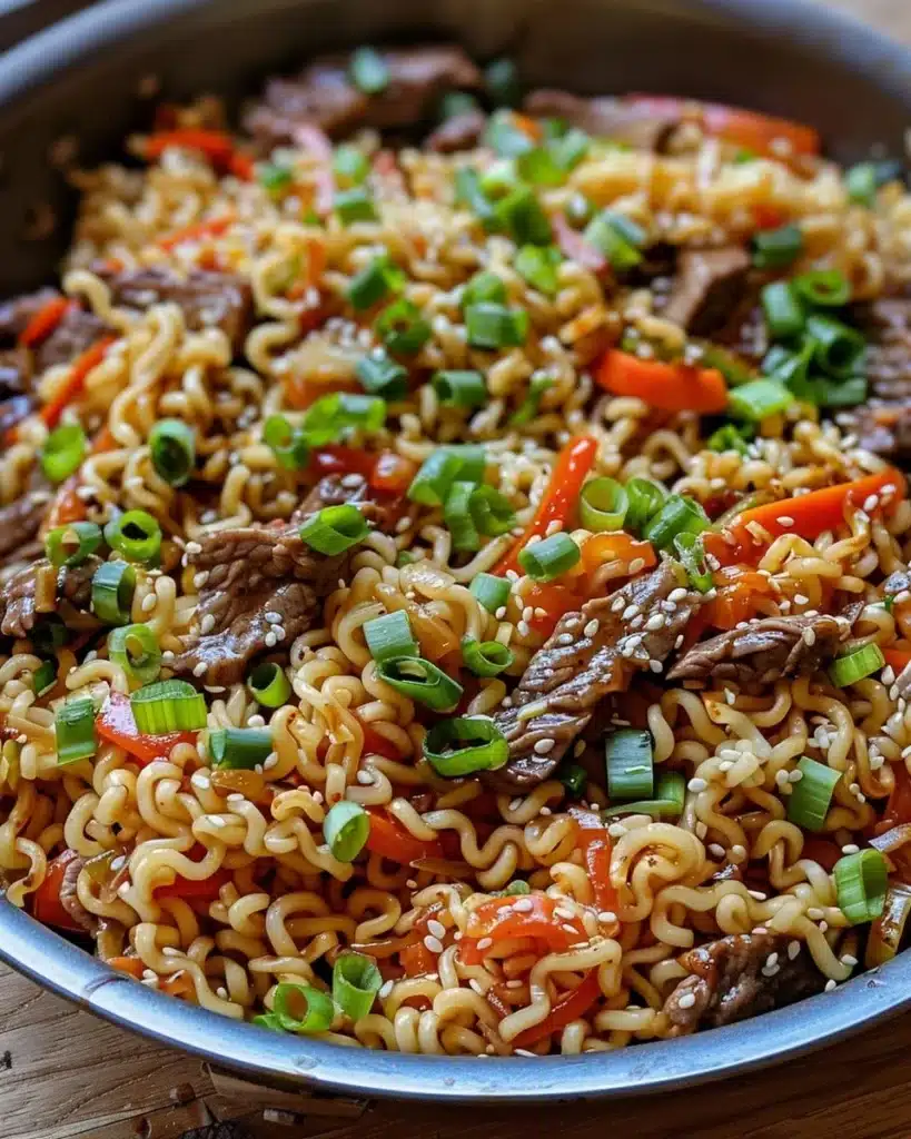 A bowl of steaming beef ramen noodles garnished with green onions and chili.