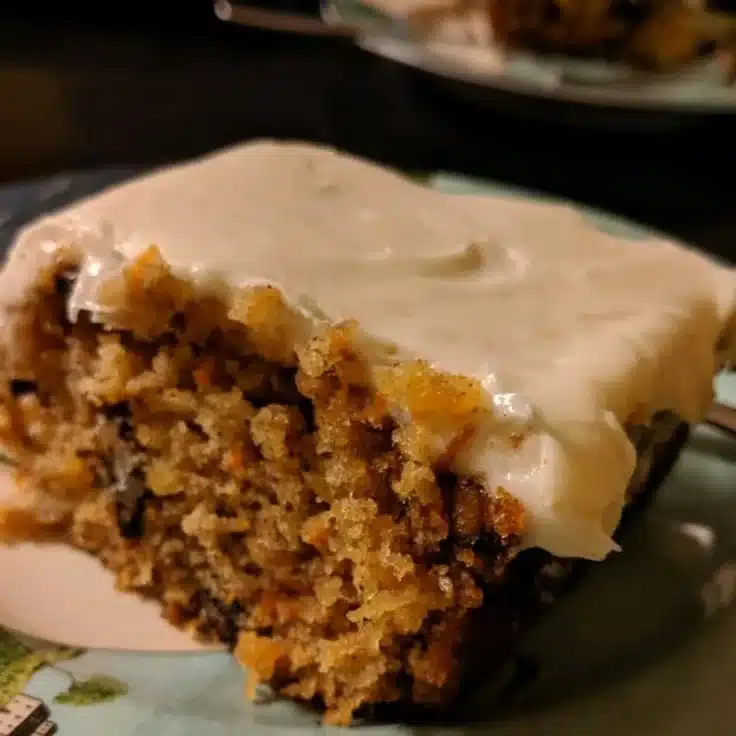 Slice of old-fashioned carrot cake with cream cheese frosting on a wooden table