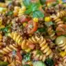 Colorful pasta salad with seasoned beef, vegetables, and dressing.