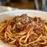 Bowl of spaghetti topped with rich meat sauce garnished with herbs