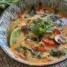 Bowl of spicy coconut curry ramen garnished with fresh vegetables and herbs