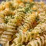 A colorful creamy cold pasta salad with vegetables and dressing in a bowl.