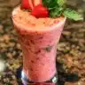 Bowl of vibrant strawberry soup garnished with fresh strawberries and mint leaves.