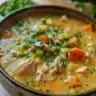 A bowl of anti-inflammatory turmeric chicken soup with fresh herbs and spices.