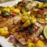 Charred Mahi Mahi fillet topped with fresh mango salsa served on a plate.