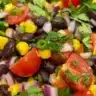 A colorful corn black bean salad served in a bowl, garnished with fresh herbs.