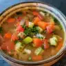 A bowl of simple vegetable soup with colorful veggies and herbs.