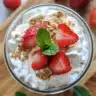 Strawberry cheesecake parfait layered in a glass with fresh strawberries and whipped cream.