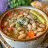 A bowl of white bean soup garnished with herbs and served with crusty bread.